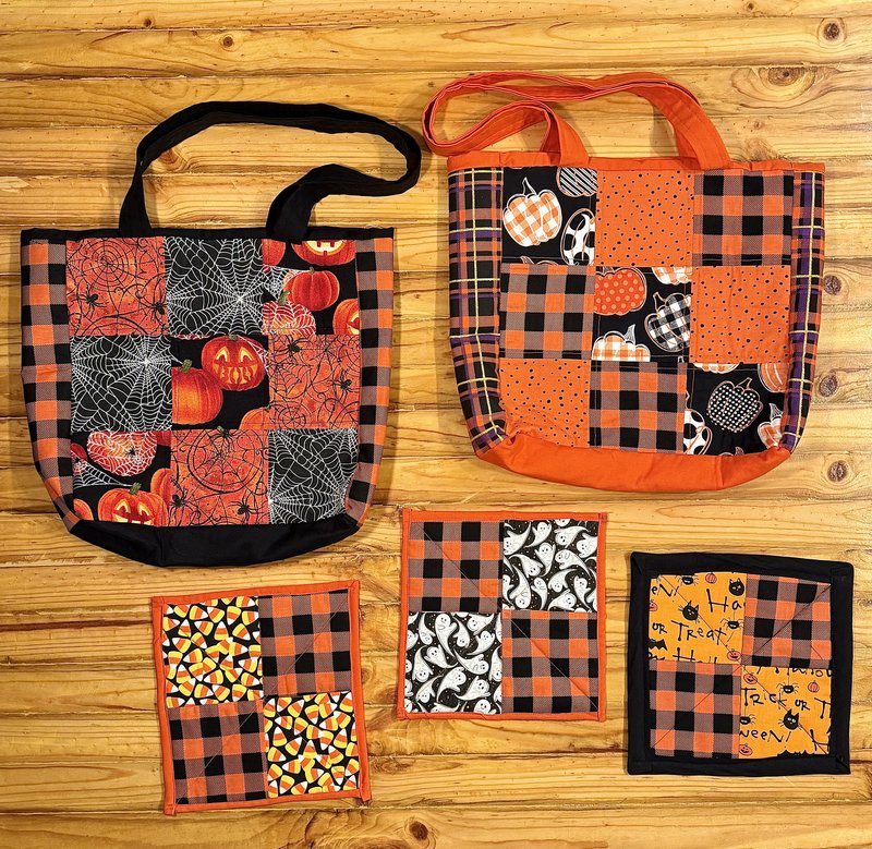 Halloween tote bags and quilted pot holders in pumpkin, ghost, and candy corn fabrics laid out on a pine table