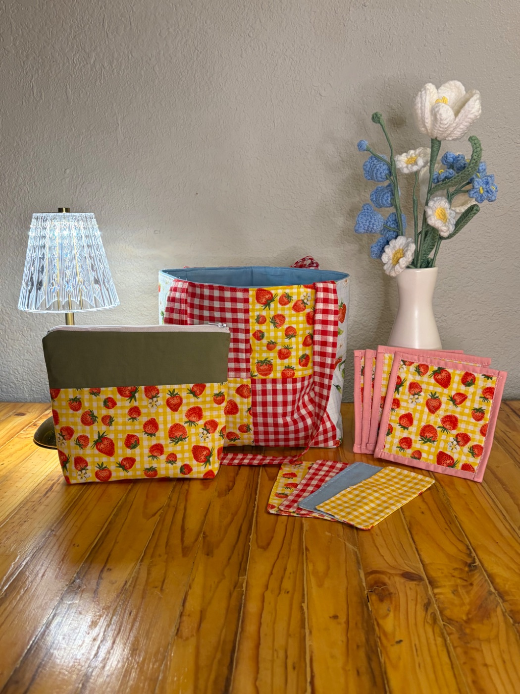 The Strawberry Picnic Bundle arranged on a wooden table with a mini tote, zipper pouch, coasters, bookmarks, and crocheted flowers